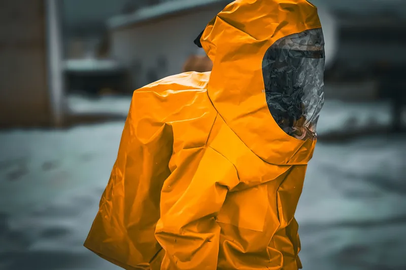 Worker in a hooded orange protective suit with a dark visor standing outdoors